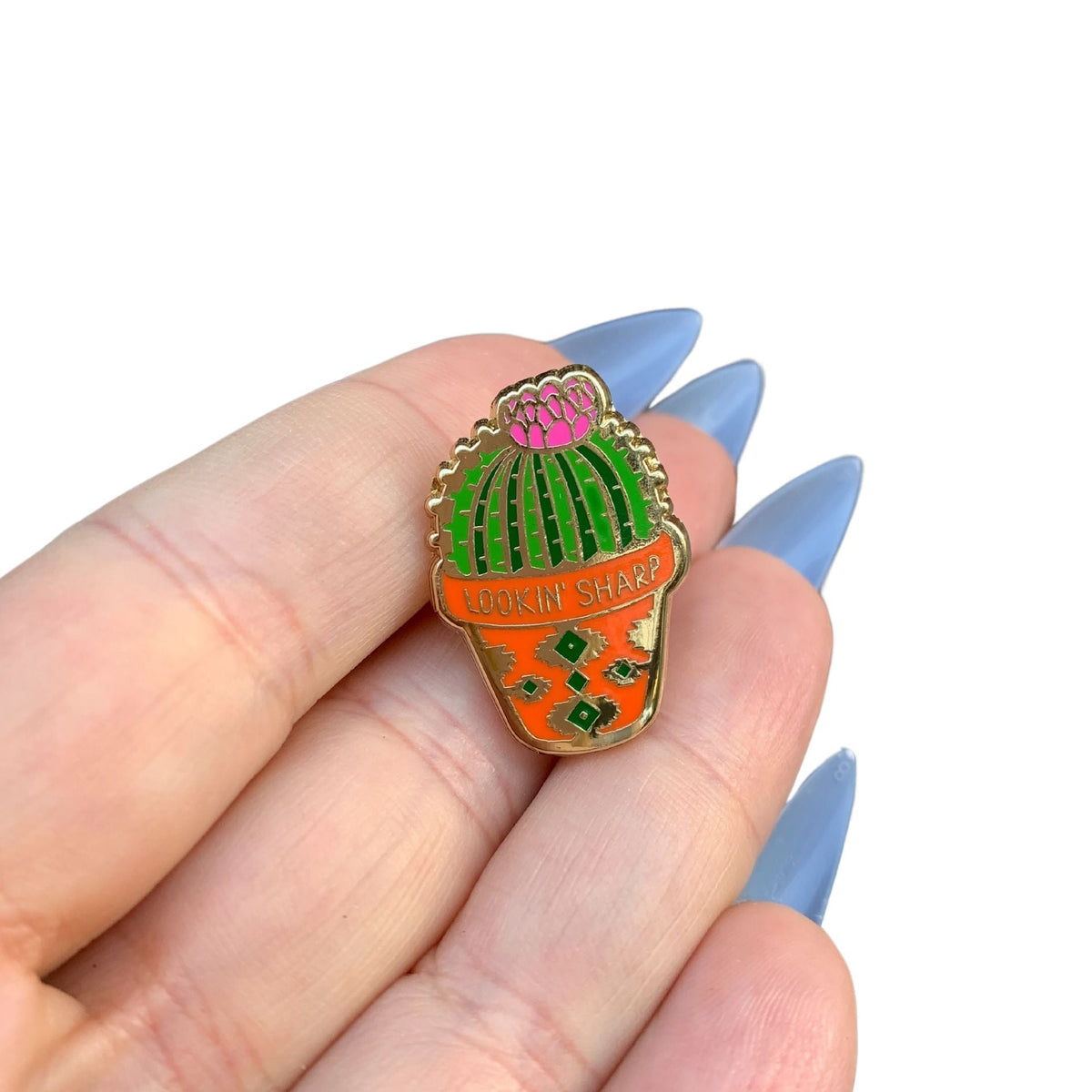 Cactus enamel pin held in hand, gold-tone frame with green and orange enamel
