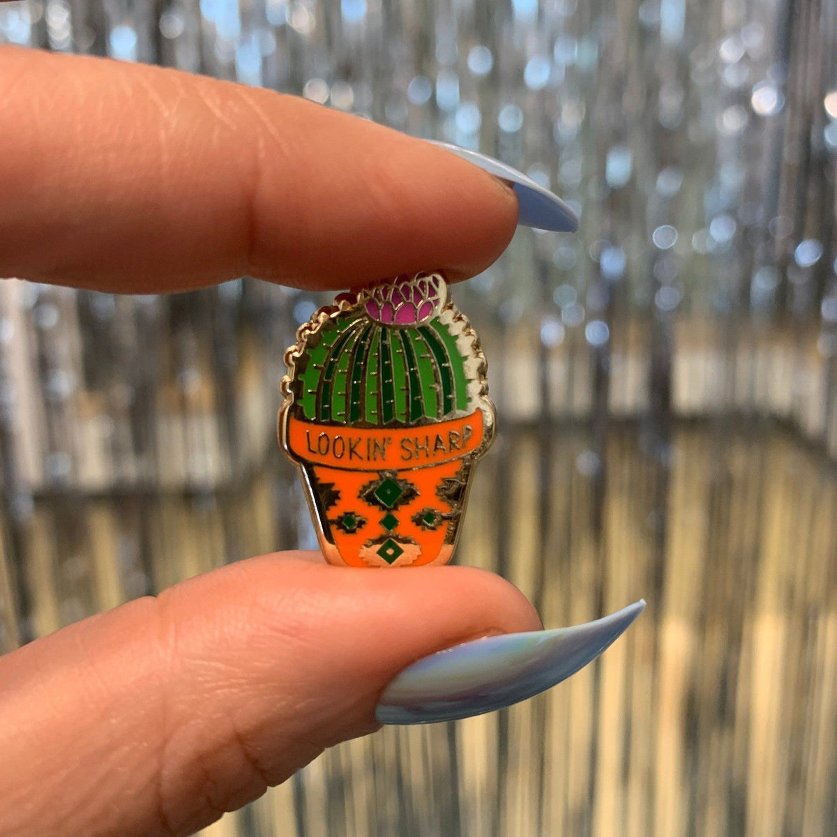 Cactus enamel pin held up outdoors, gold-tone cactus design with orange base