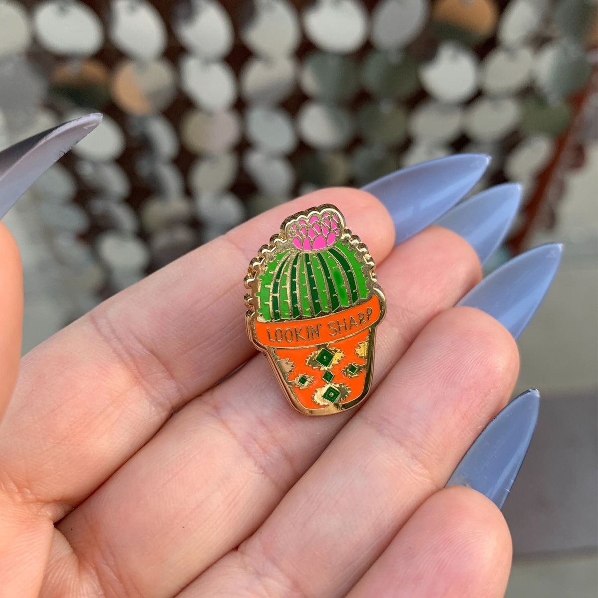 Cactus enamel pin in open palm, green top with orange bottom and gold-tone edge
