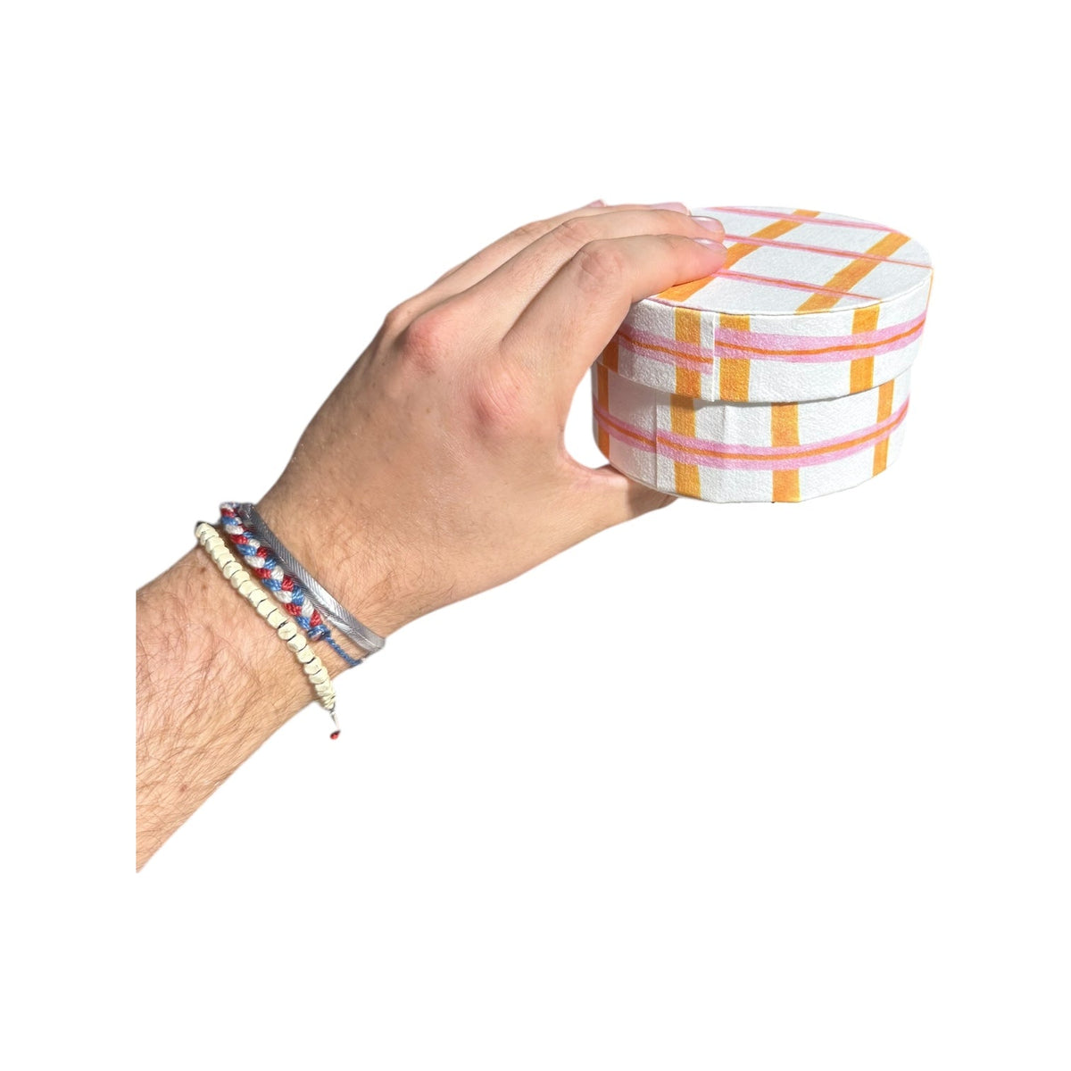 Hand holding a round handmade recycled paper gift box with white base and orange plaid stripes.