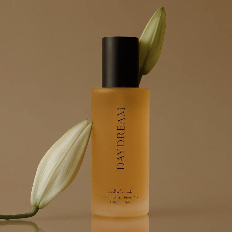 Amber body oil bottle with black pump, DAYDREAM branding, with green leaf.