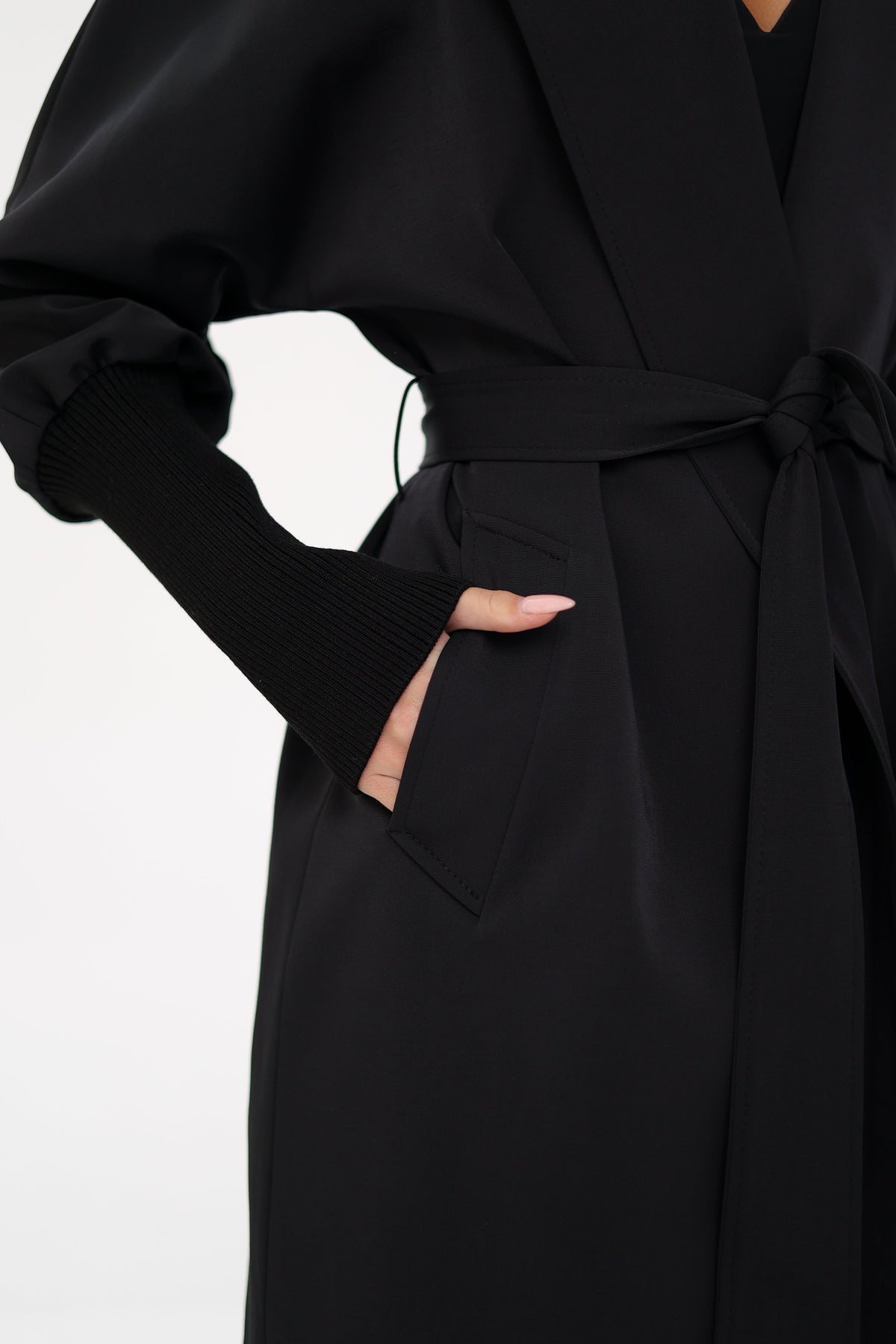 Black trench coat detail with tie belt, side pocket, and ribbed cuff