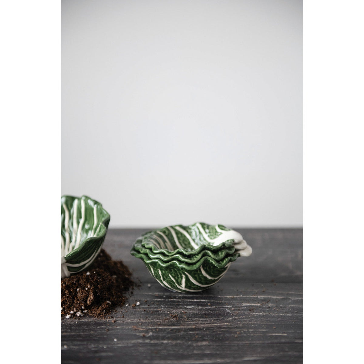 Cabbage-shaped nesting bowl, glossy green with white veining, on a dark board.
