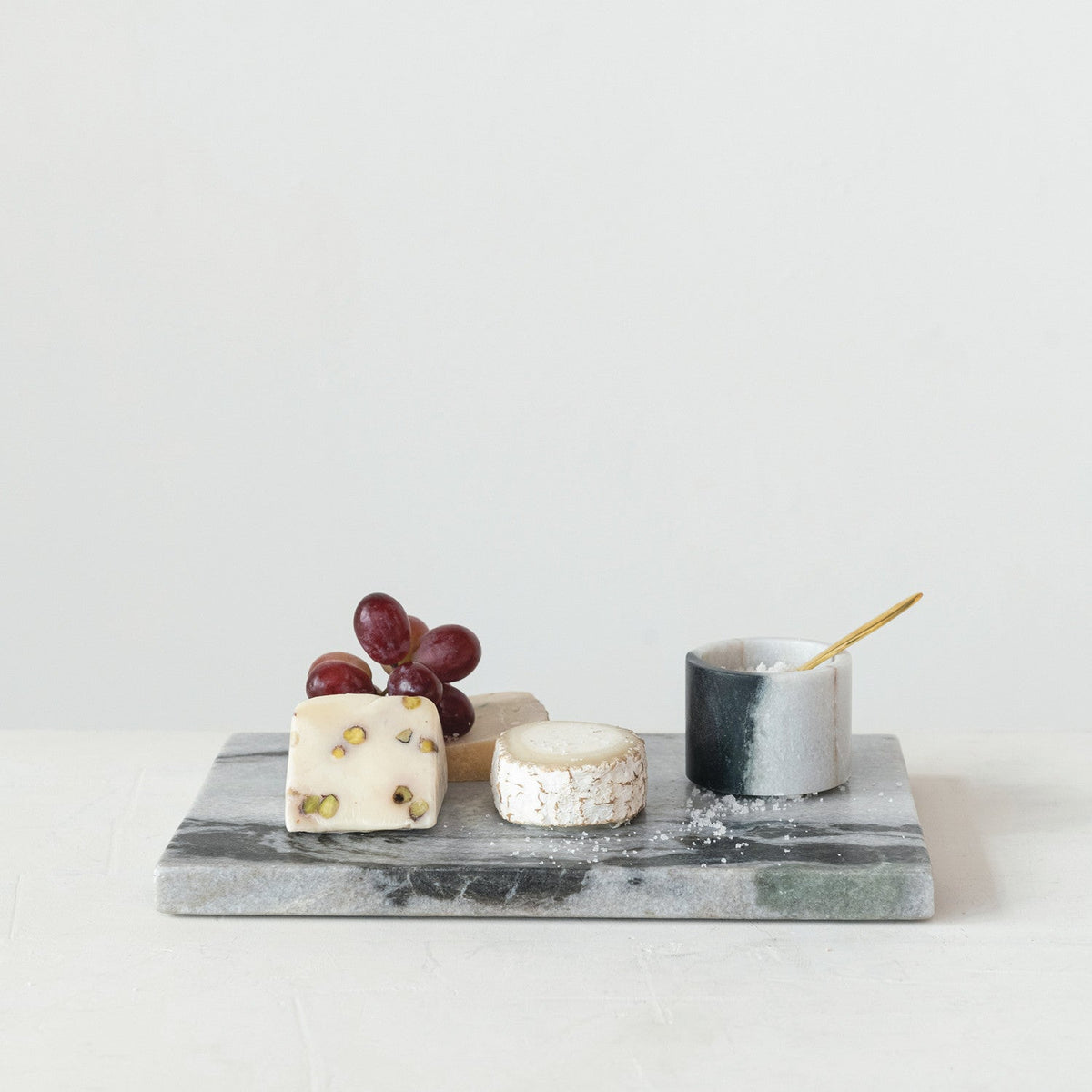 Marble salt cellar cup on gray stone tray with brass spoon