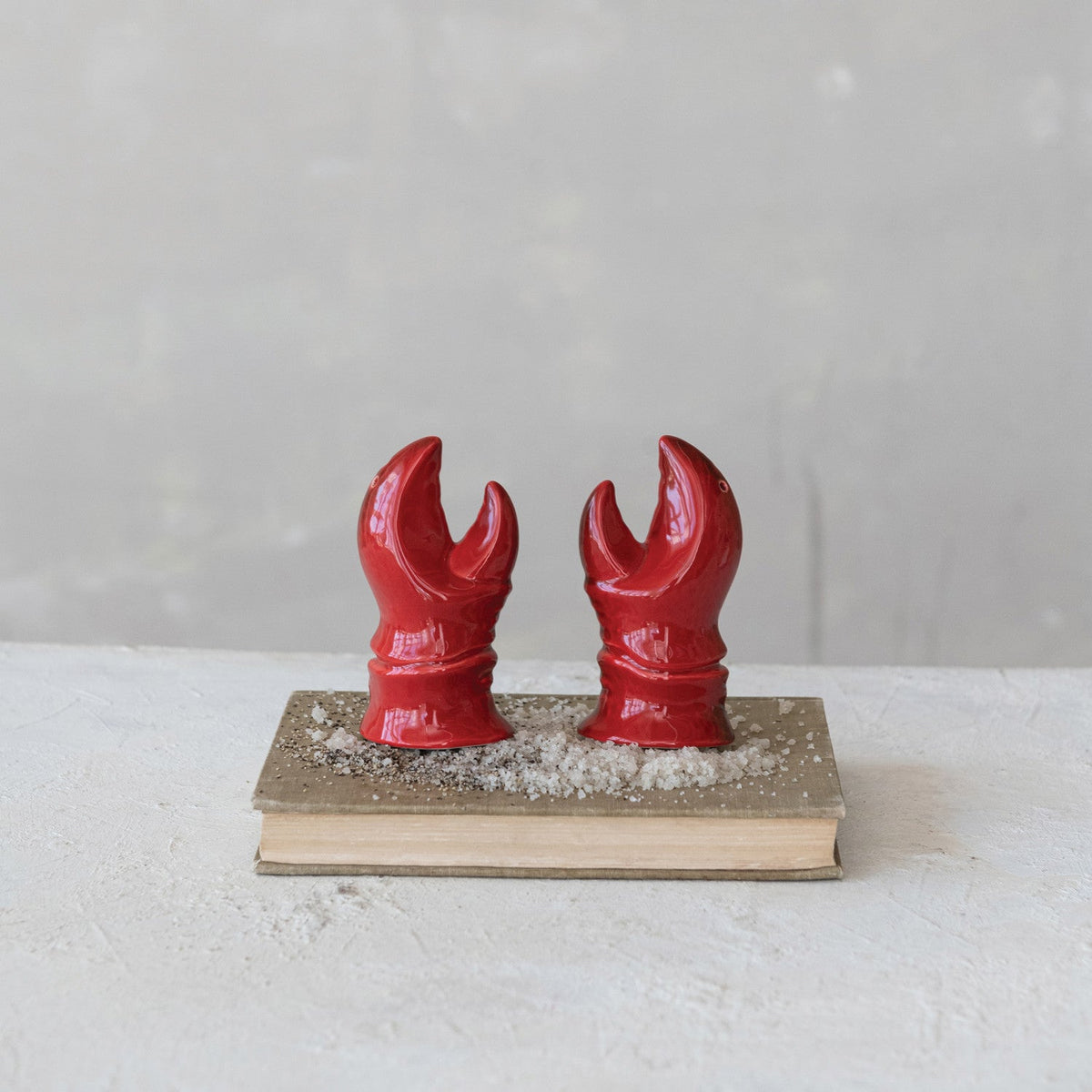 Two red lobster claw salt and pepper shakers on a small wooden base