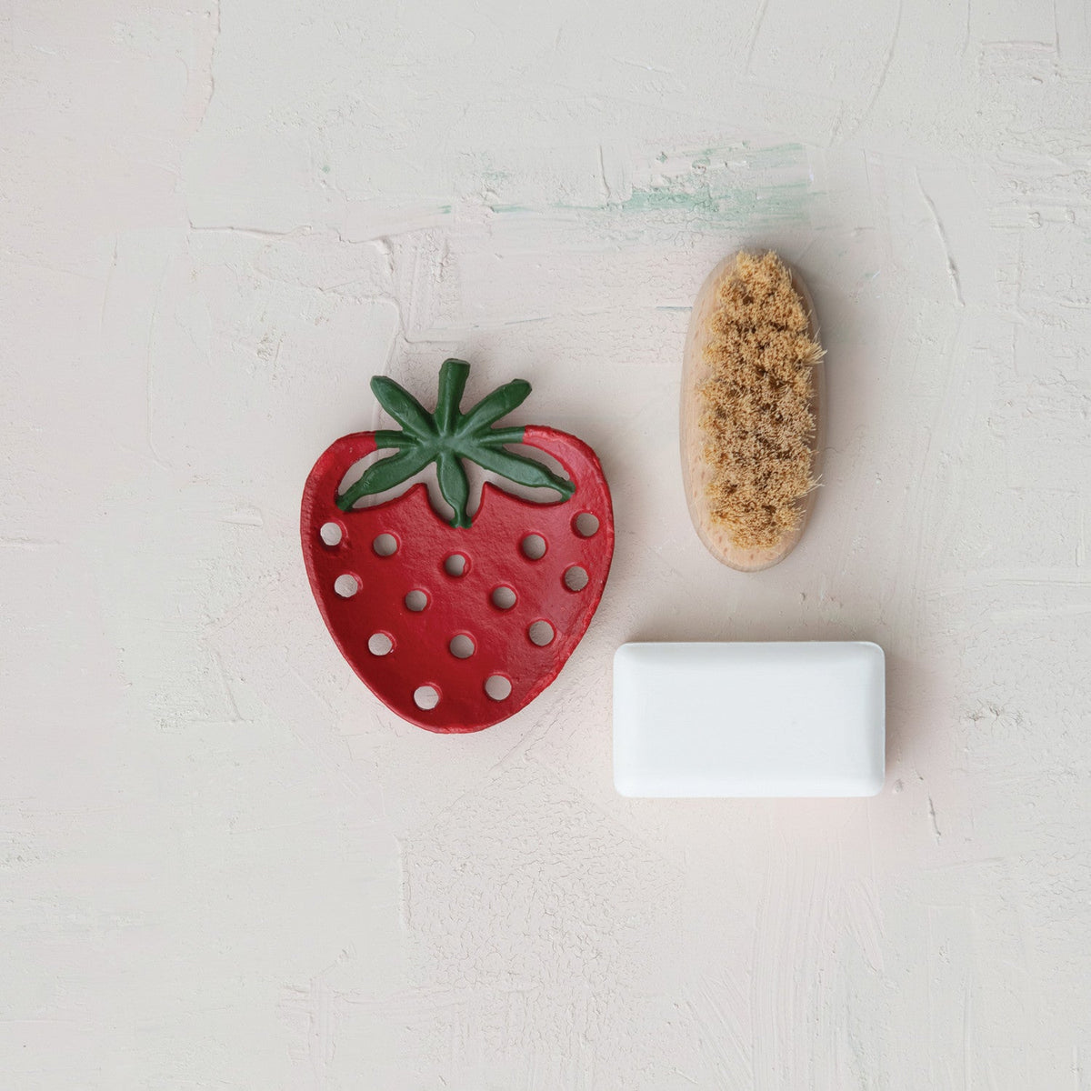 Red strawberry-shaped cast iron soap dish with drainage holes, with soap bar nearby