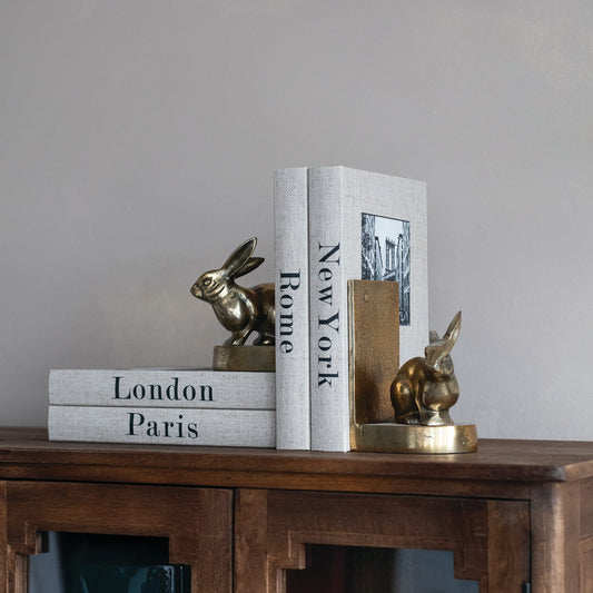 Antique gold rabbit bookends holding upright books on a shelf