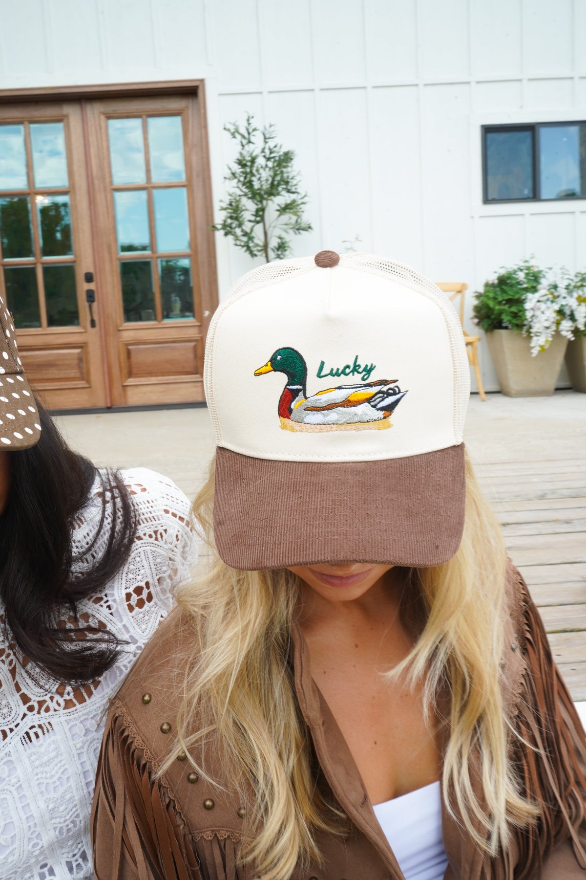 Close-up of cream trucker hat with brown corduroy brim and duck “Lucky” front logo.