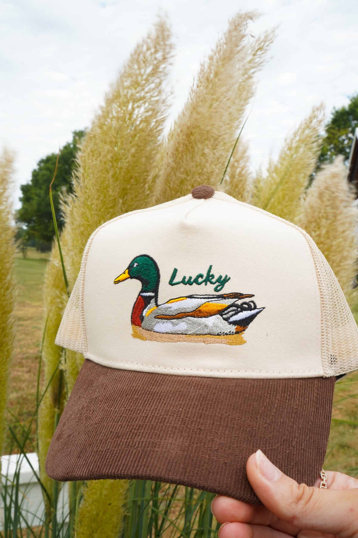 Close-up front of brown corduroy trucker hat with cream mesh and Lucky duck logo