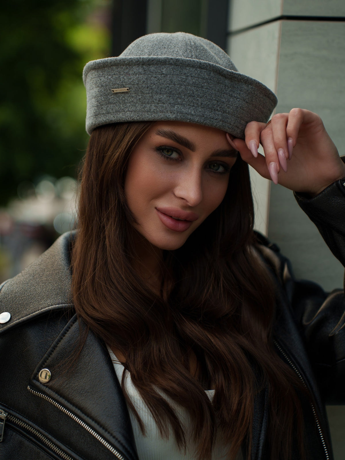 Light grey sailor hat with a rounded crown, wide band and small gold-tone pin, worn on a model