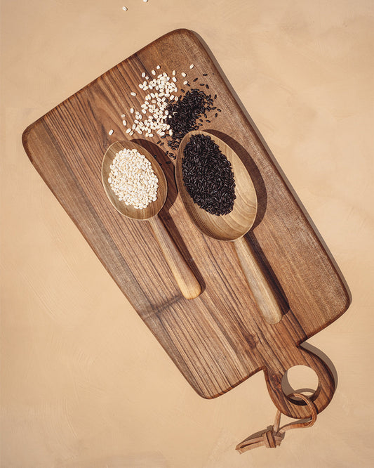 Two walnut scoop spoons on wood tray, filled with light and dark grains