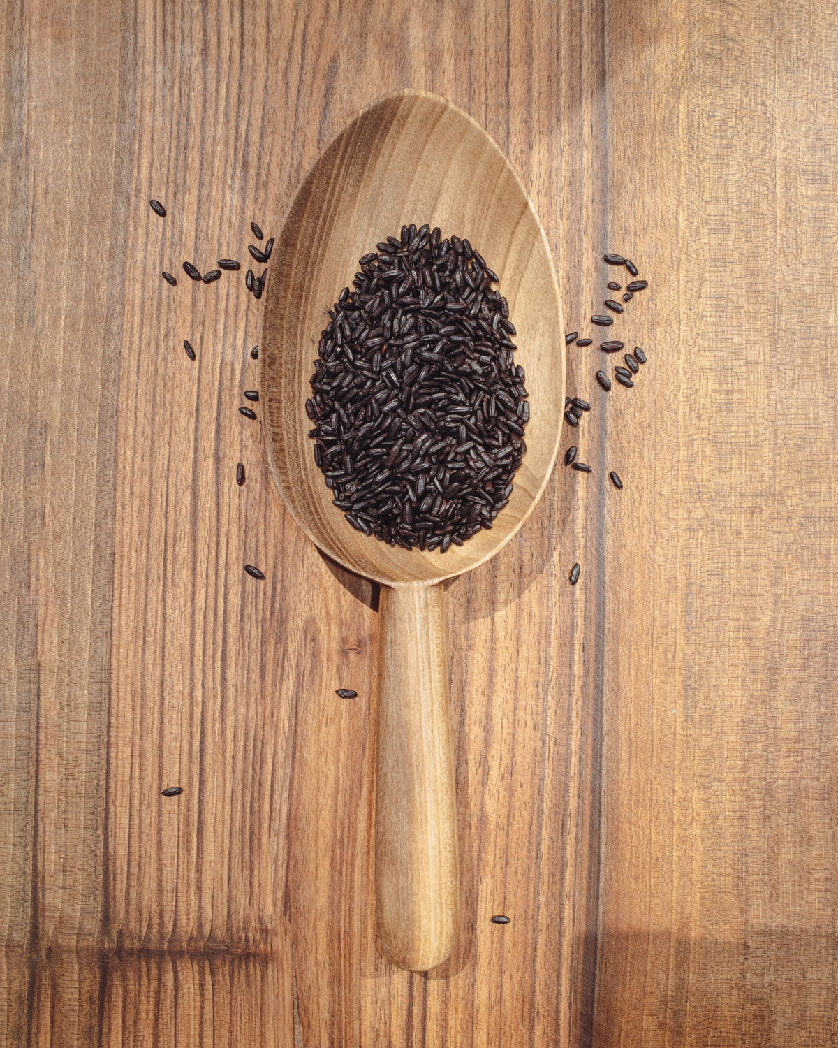 Walnut scoop spoon with dark grains in oval bowl on wooden board