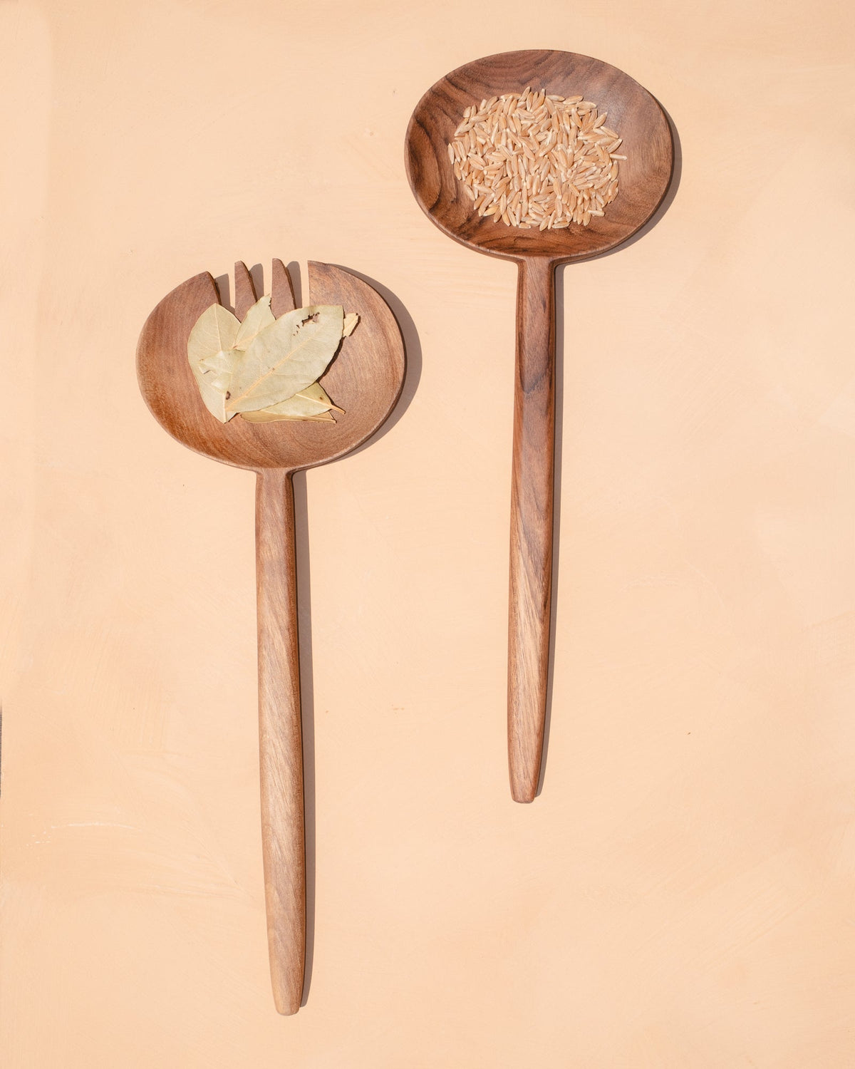 Wooden oval salad serving spoons with forked tines, filled with salad