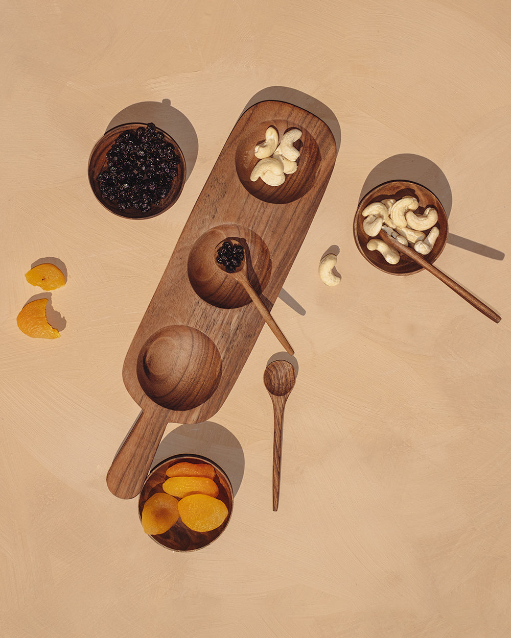 Carved wooden condiment board with three bowls and multiple spoon utensils
