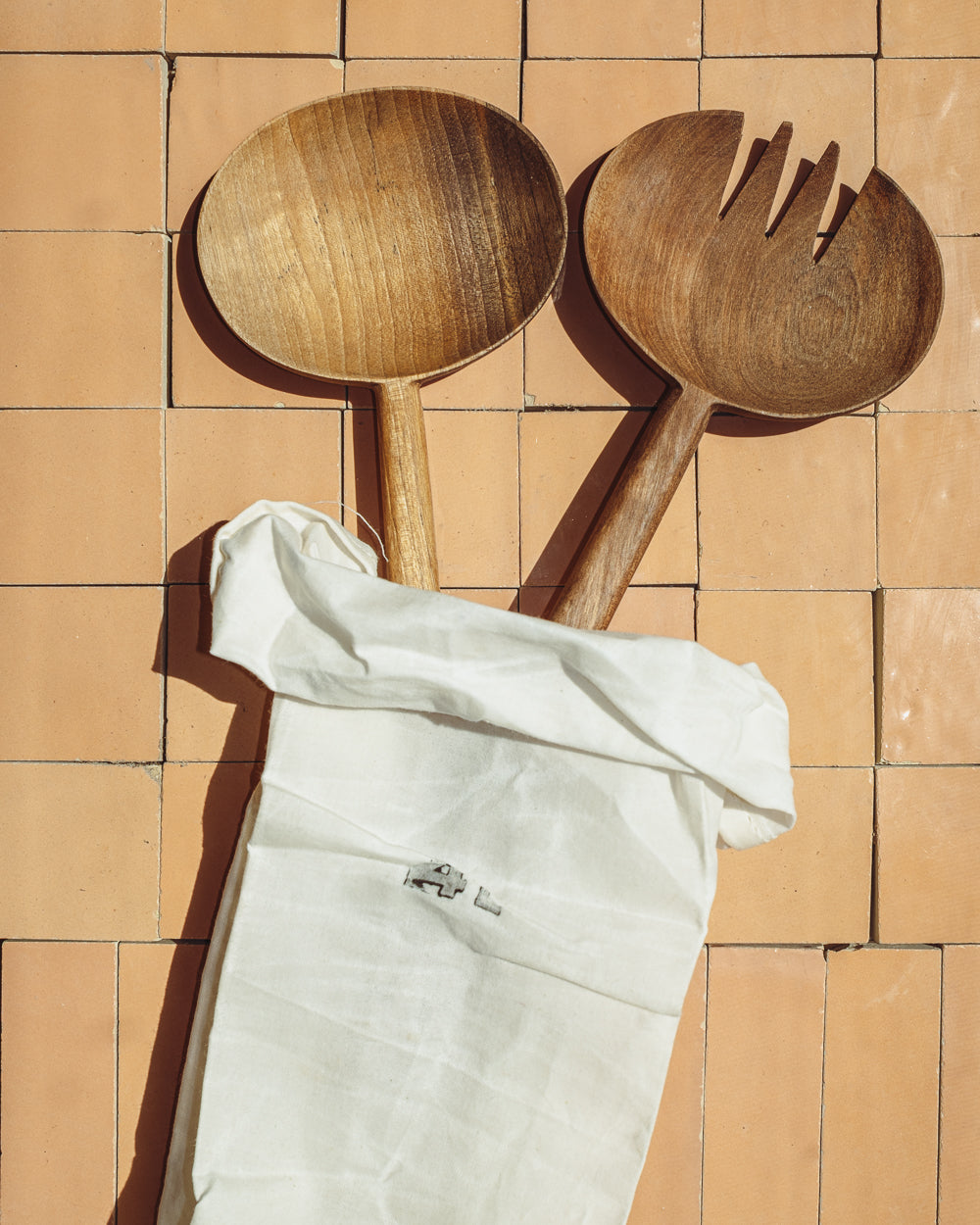 Wooden oval salad serving spoons with forked tines, beside a white storage bag