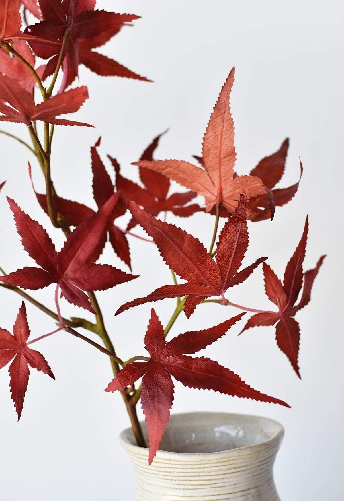 Faux Japanese maple leaf stem with red leaves arranged in a white ribbed vase