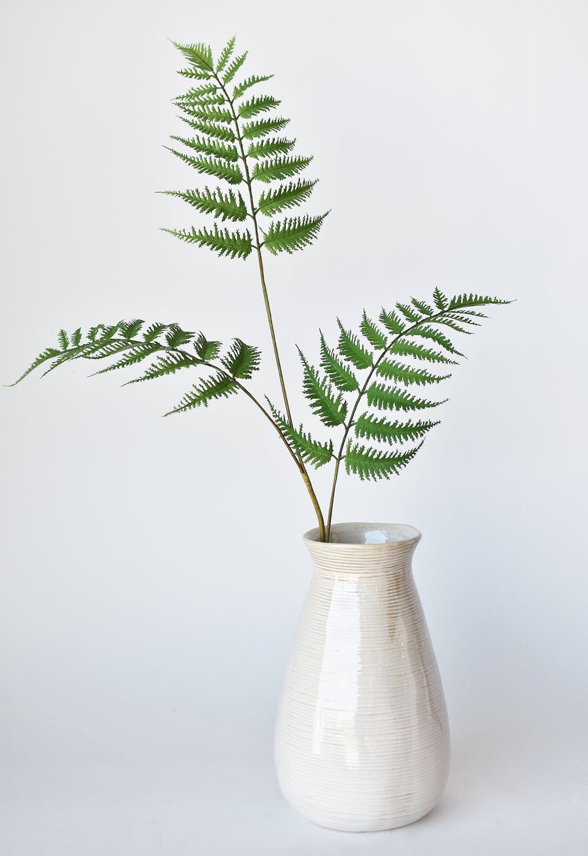 Faux forest fern spray in a white textured vase with multiple green fronds