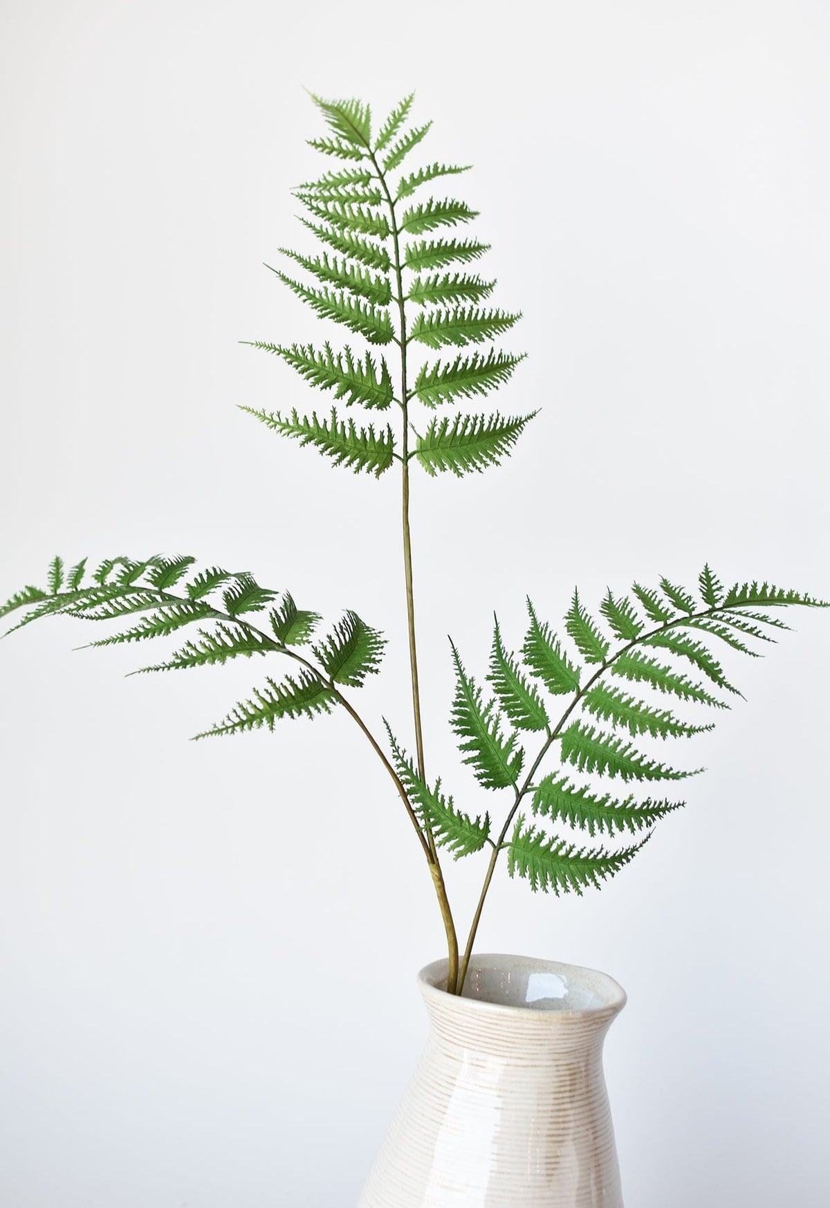 Faux forest fern spray in a white textured vase with green fronds and stems