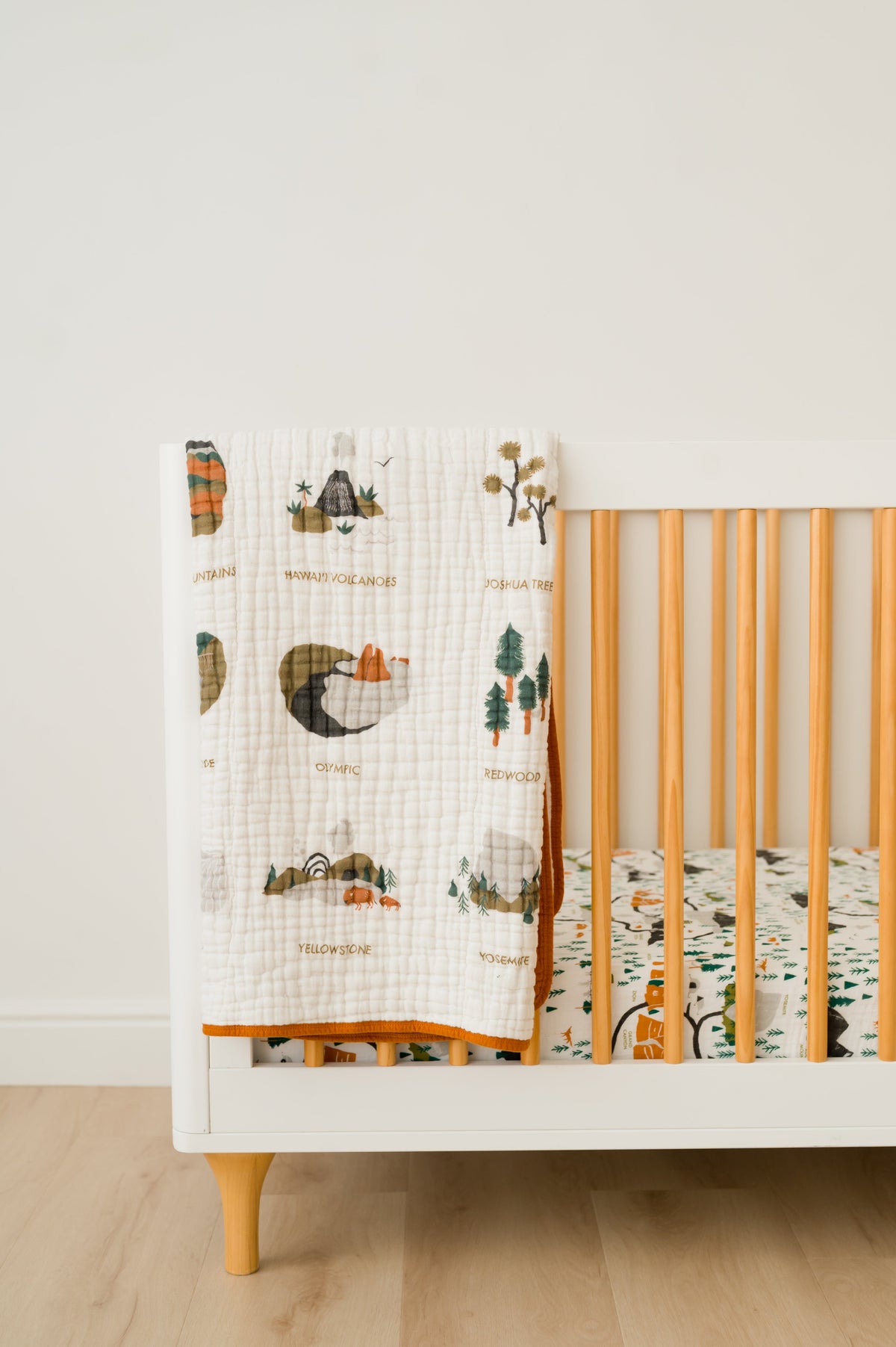 White muslin blanket with orange border and illustrated national parks prints on a crib