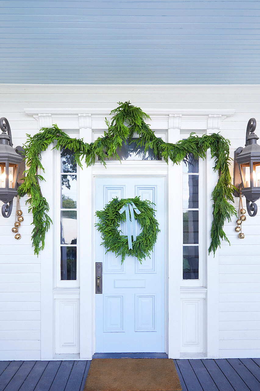 Green faux pine Christmas wreath centered on a porch entry door.