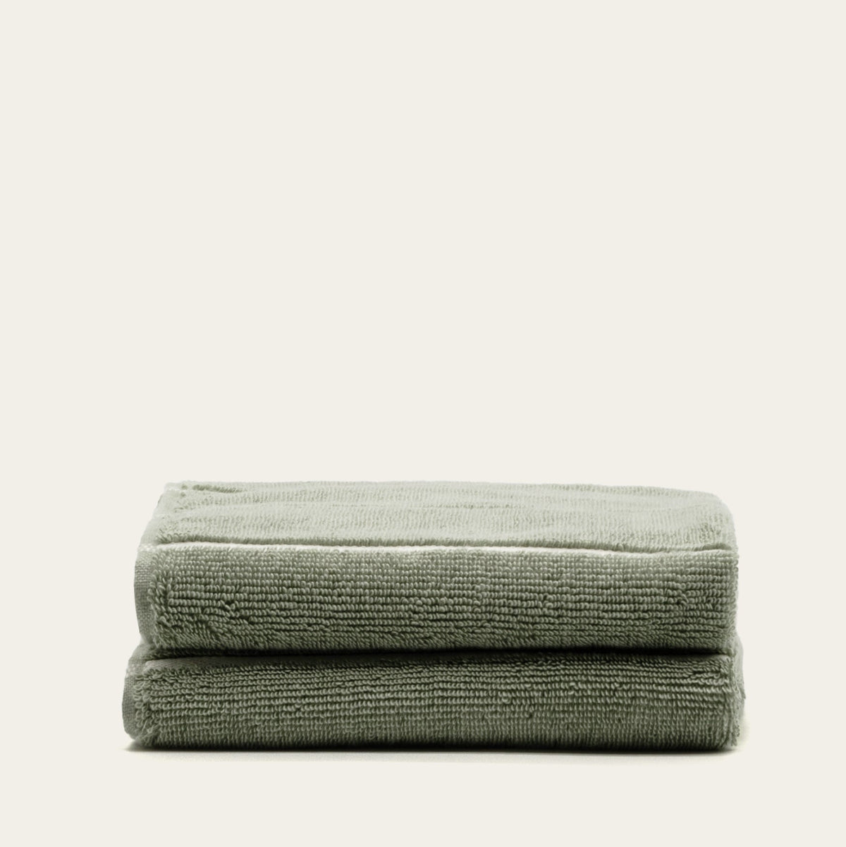 Sage green cotton towels with ecru border, folded in a stack of two