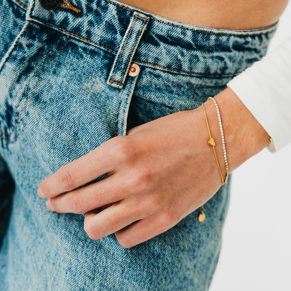 Gold bracelet with round charm and silver tennis bracelet with bead links on wrist