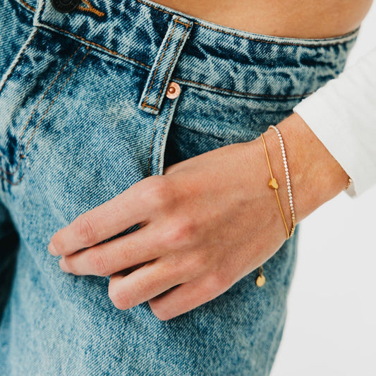 Gold bracelet with round charm and silver tennis bracelet with bead links on wrist