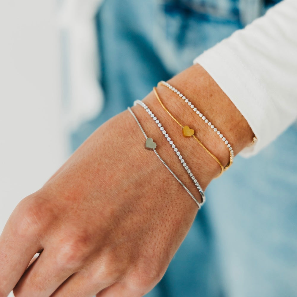 Gold and silver tennis-style bracelets with small round disc charms on a wrist