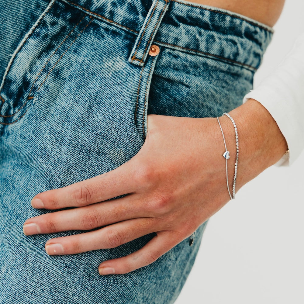Silver tennis-style bracelet with small round disc charm on wrist