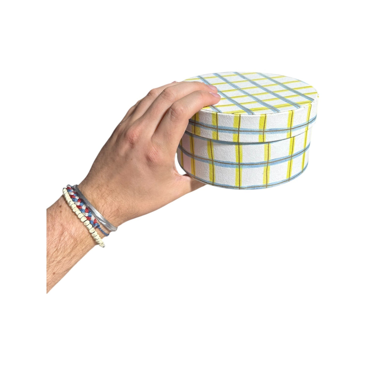 Hand holding a round handmade recycled paper gift box with green and blue plaid stripes.
