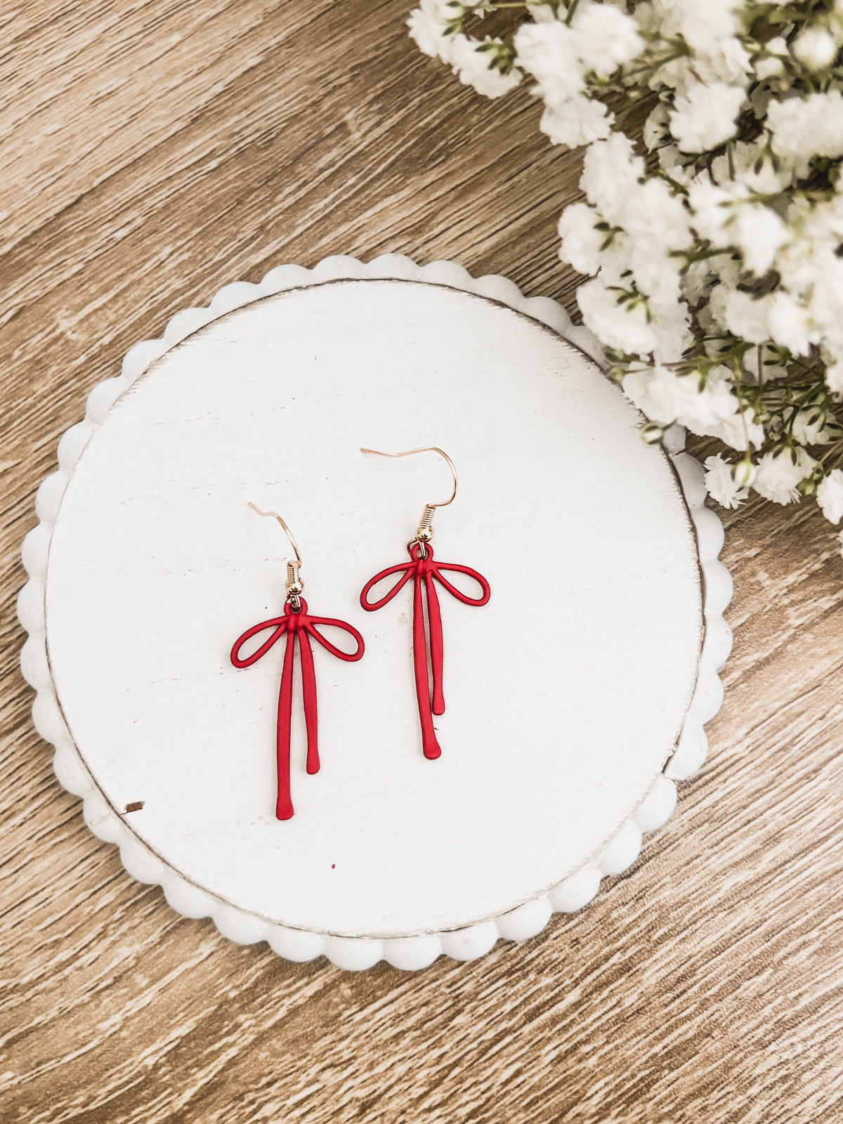 Red bow drop earrings with dangling tassels and gold-tone hooks on a white round card