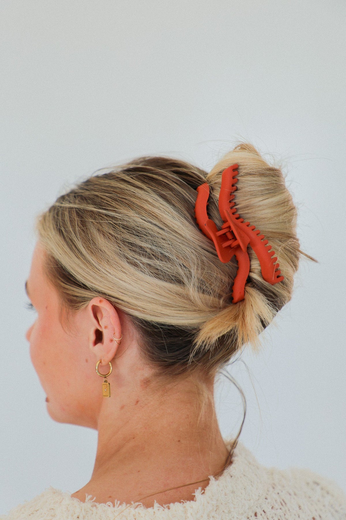 Wavy midi claw hair clip holding a bun, highlighted hair, red-orange clip