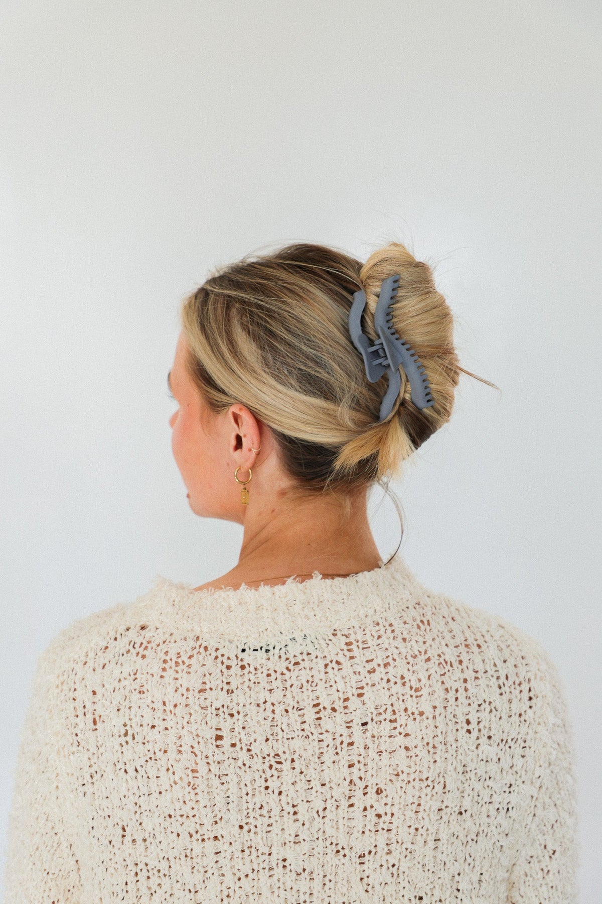 Wavy midi claw hair clip holding a bun, light hair, blue clip
