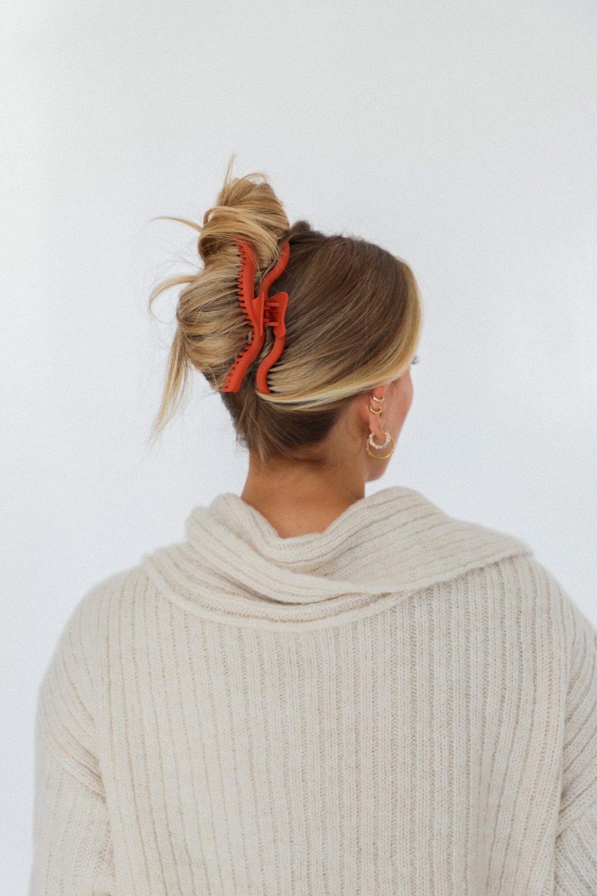 Wavy claw hair clip in warm orange-red securing a bun from the side