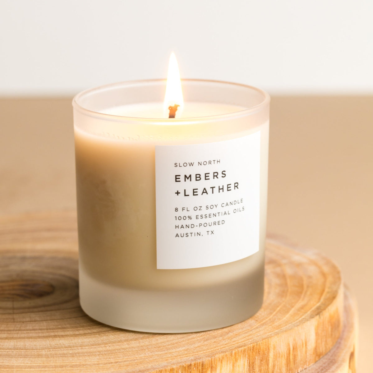 Lit Embers + Leather soy candle in a frosted glass tumbler with a white label.