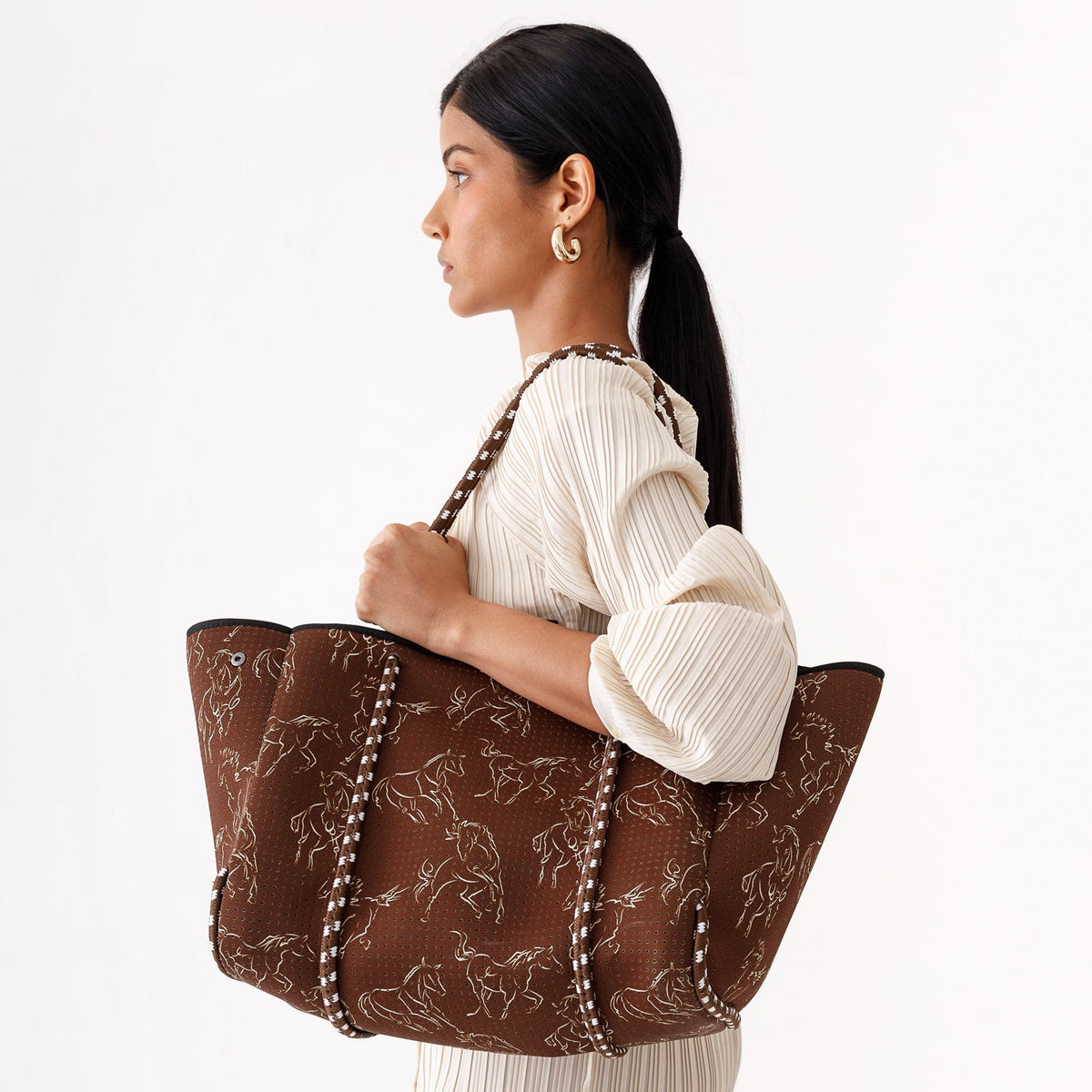 Brown horse-print tote bag with striped handles, shown being carried over the shoulder