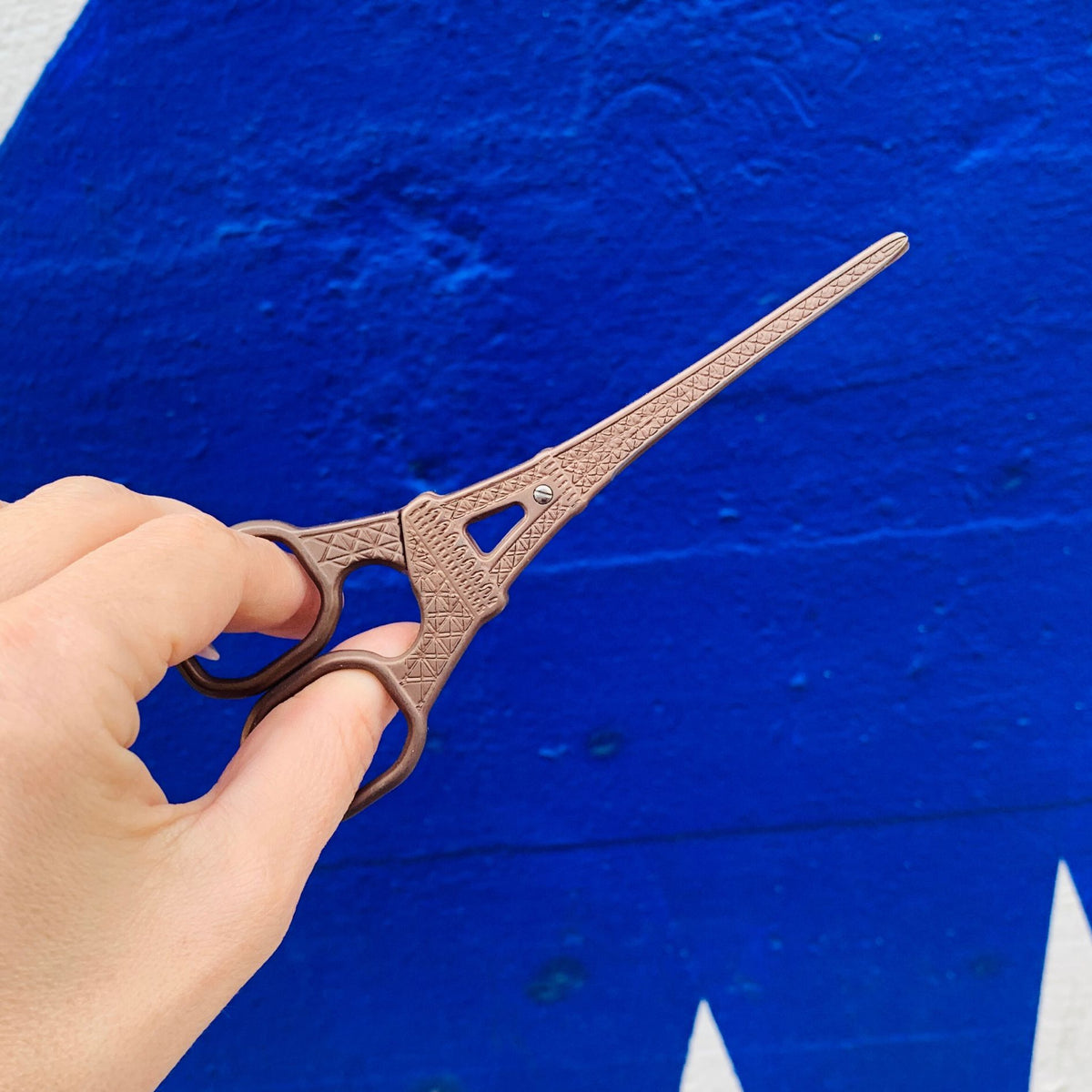 Eiffel Tower mini scissors held by hand, gold-toned metal, side view with two finger loops.