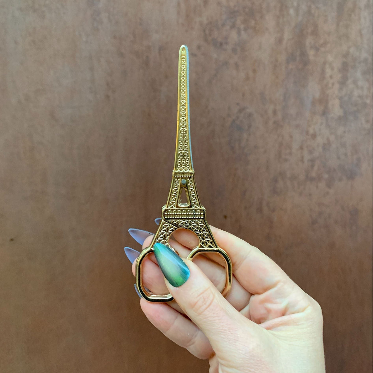 Eiffel Tower mini scissors held in hand, gold-toned metal, upright view, two finger loops.
