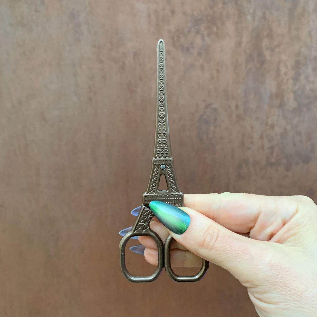 Eiffel Tower mini scissors held in hand, antique silver metal finish, upright view, two loops.