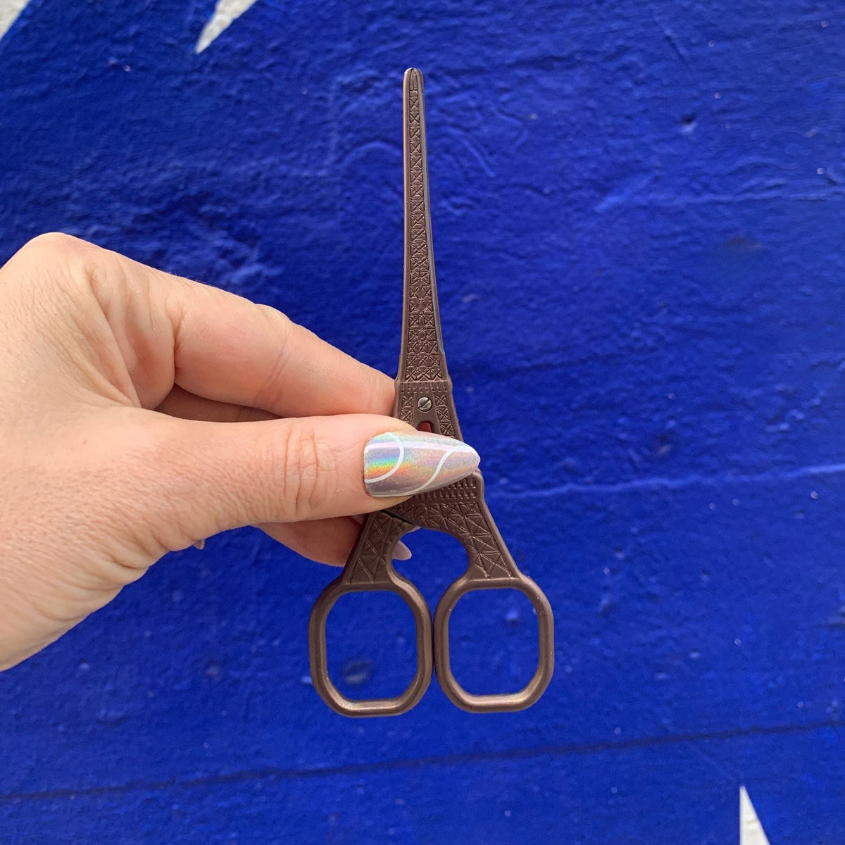 Eiffel Tower mini scissors held by hand, bronze metallic finish, front view, two finger loops.