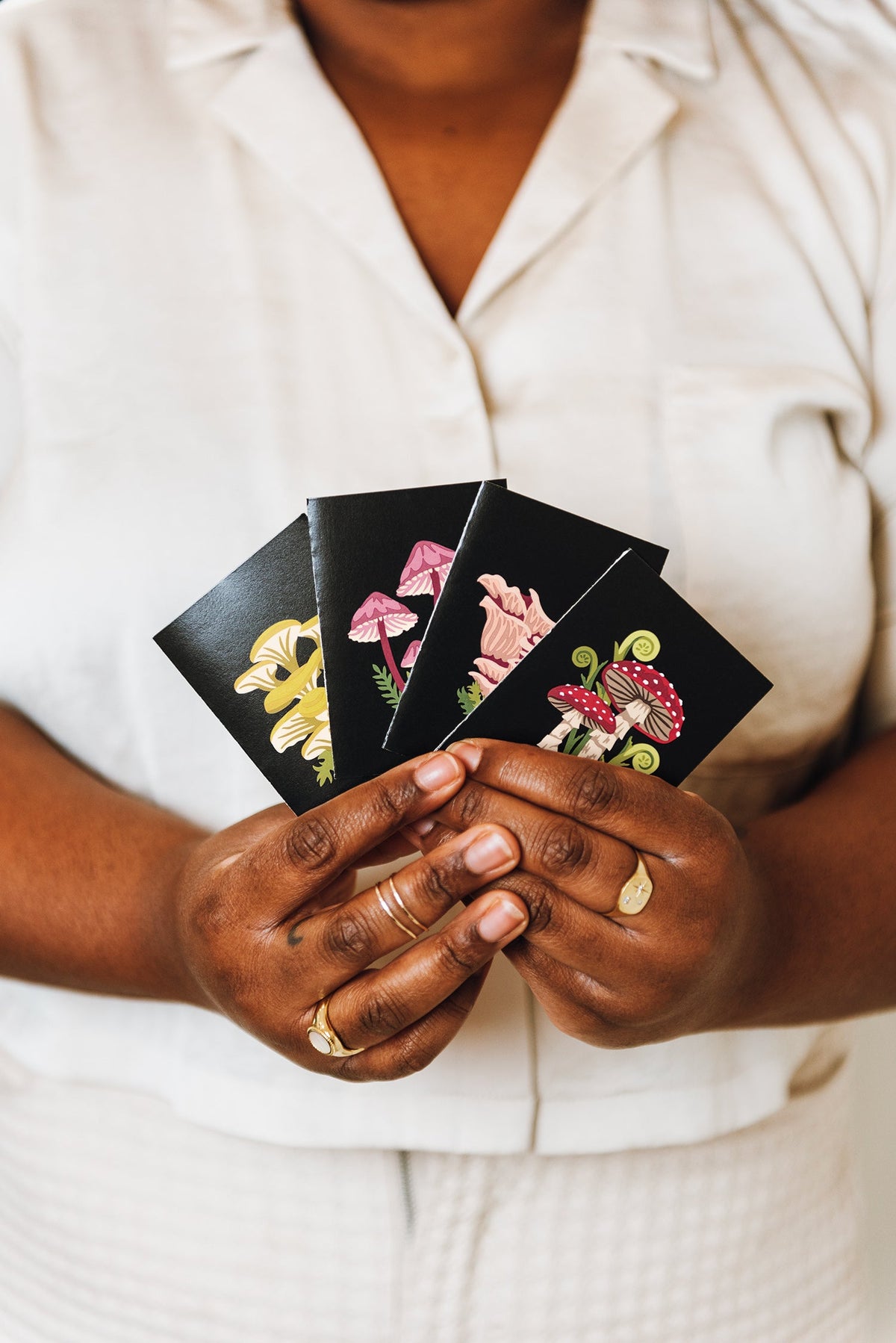 Hands holding mini mushroom cards: black cards with yellow and pink mushroom art
