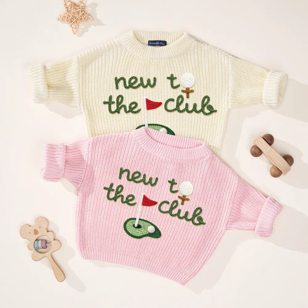 Two knit golf sweaters (cream and pink) with 'new to the club' embroidered golf flags