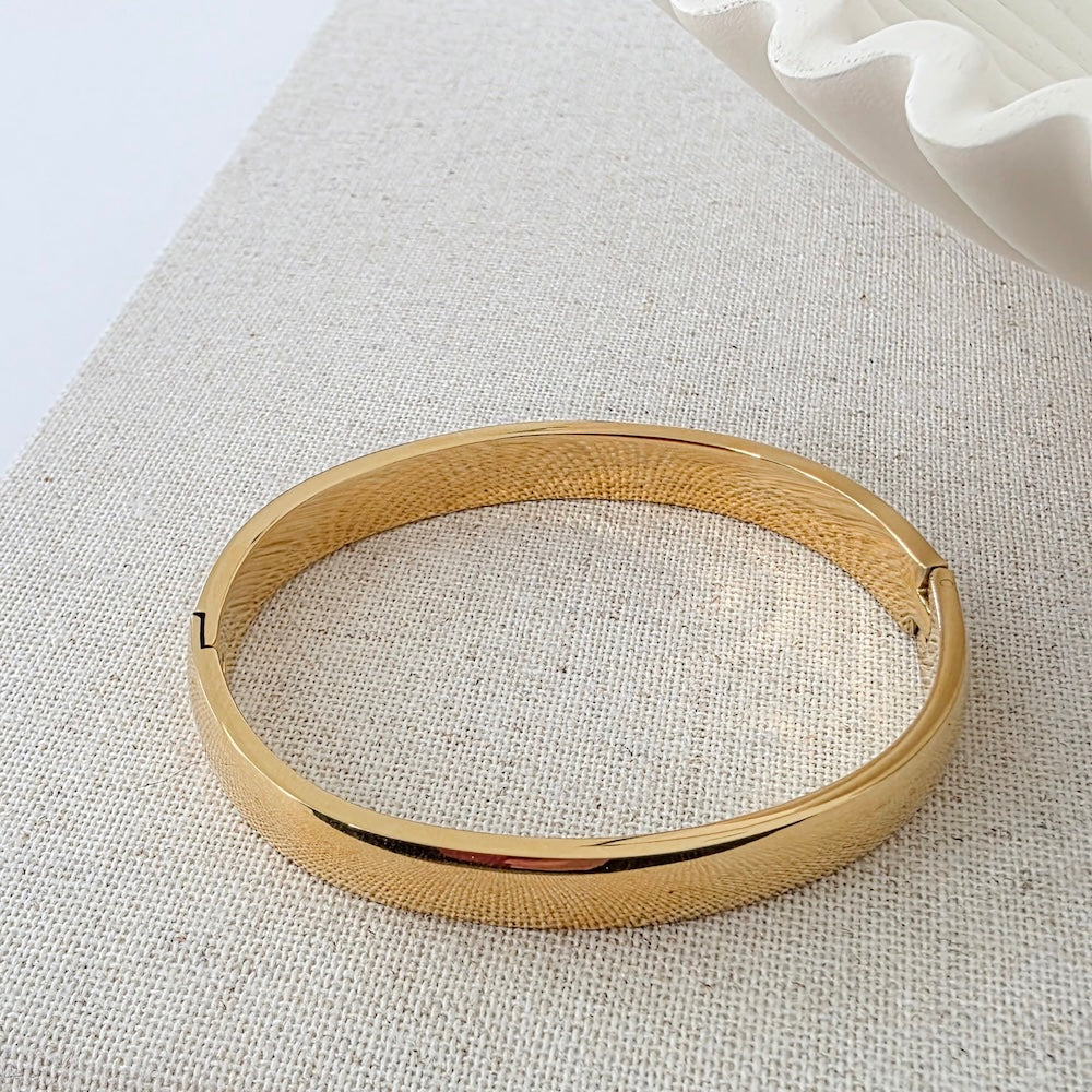 Gold-tone round hinged bangle bracelet, shown flat on fabric surface