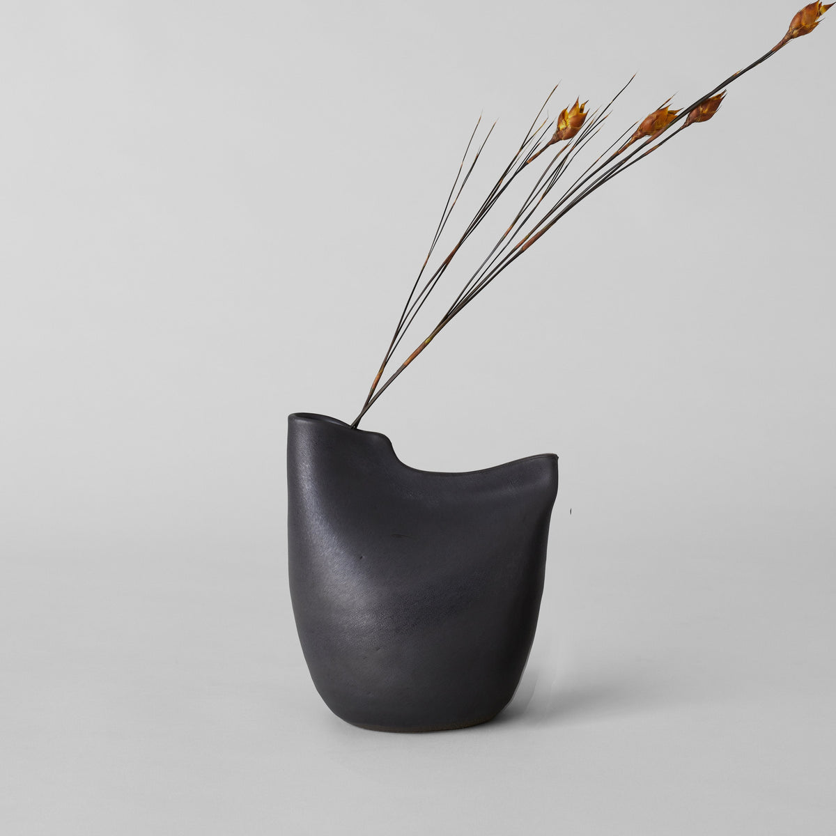 Matte black bird vase with open top and arched silhouette, with dried stems.
