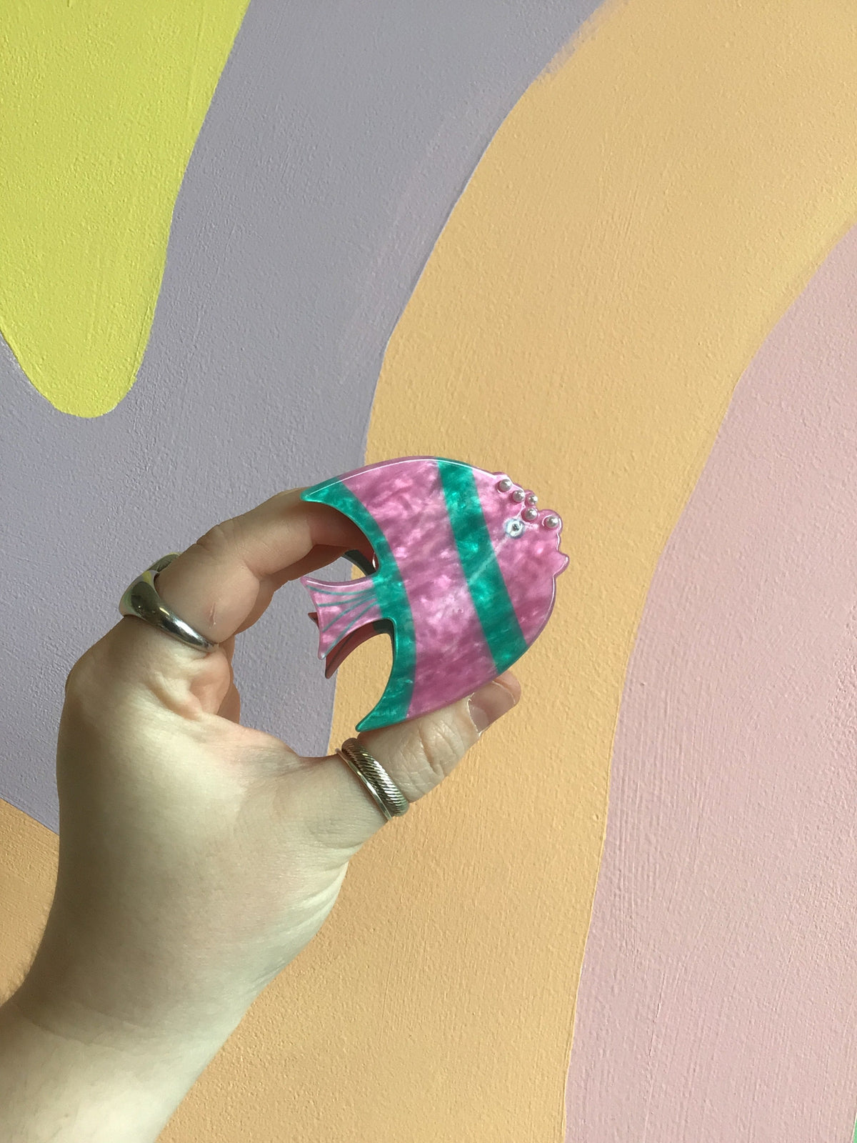 Pink and purple fish-shaped hair claw with green-and-teal stripe accents