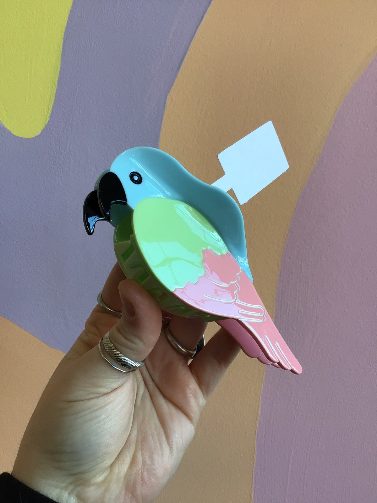 Parrot-shaped hair claw with blue head, mint green wing, and pink tail, glossy