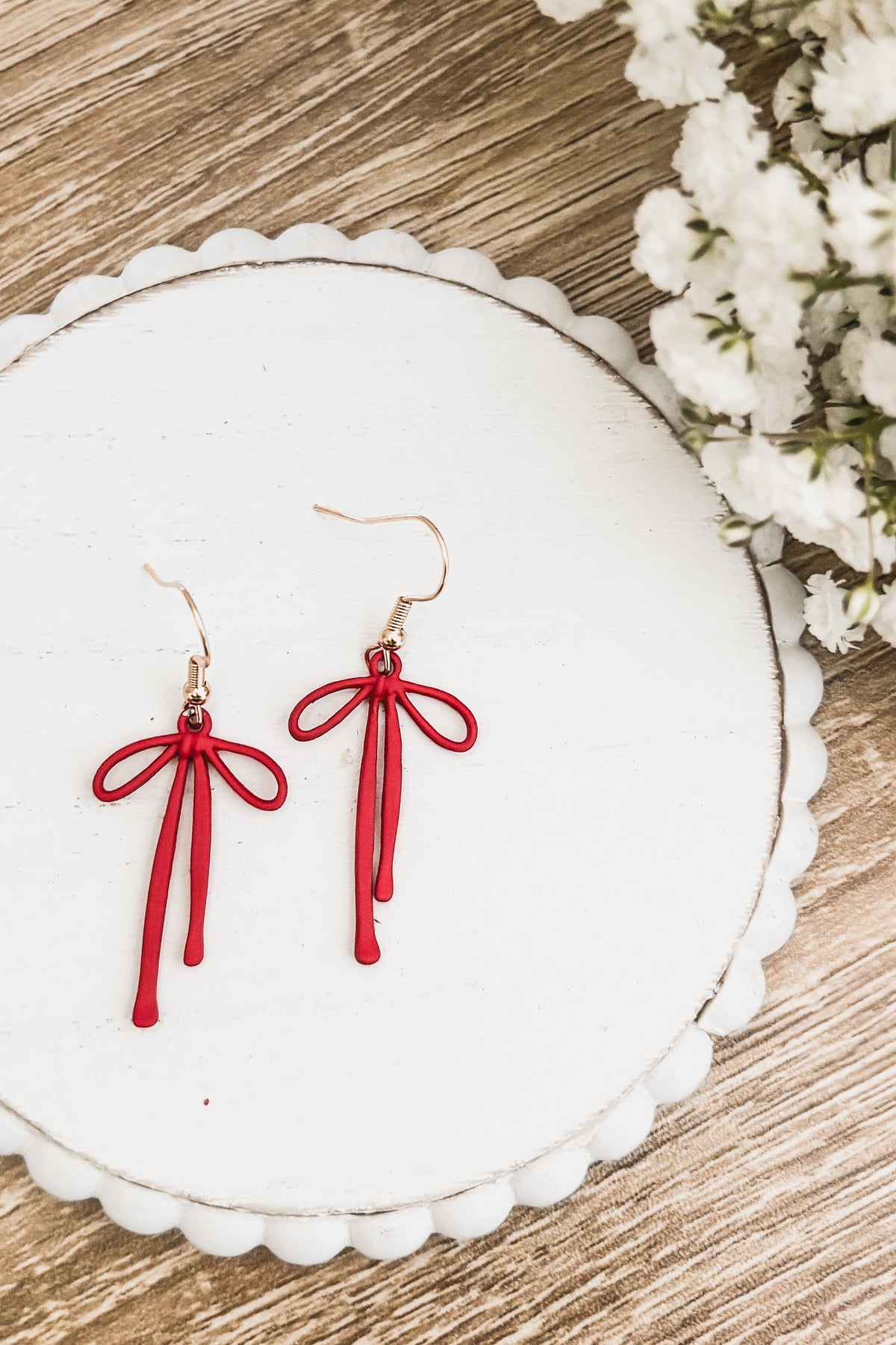 Red bow drop earrings with tassel strands and gold-tone hooks on a white round card