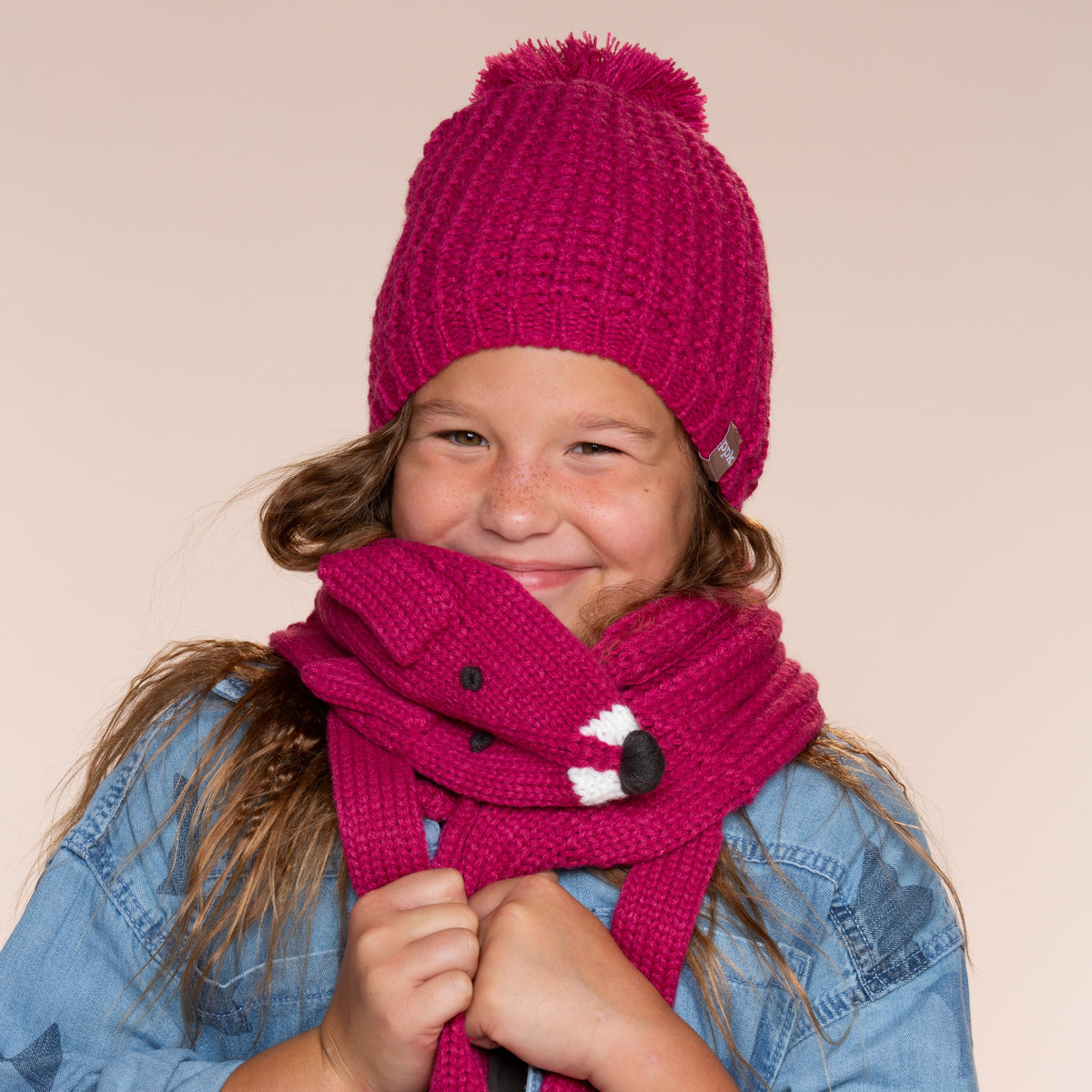 Pink knitted fox neck warmer worn by a child, with snap button and dangling ends