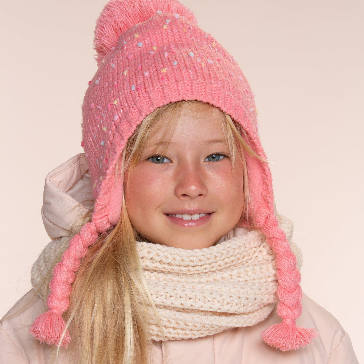 Pink flecked knit earflap hat with pom-pom and braids, worn from the front