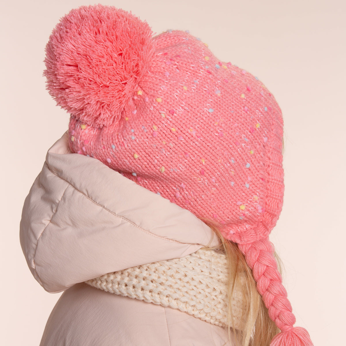Pink knit earflap hat with pom-pom and braided ties, shown from the side